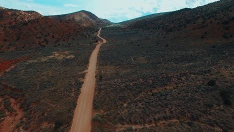 dramatic aerial forward tilt up over dirt road leading through empty savanna