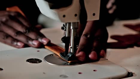 black hands operate a sewing machine to sew together a leather strap