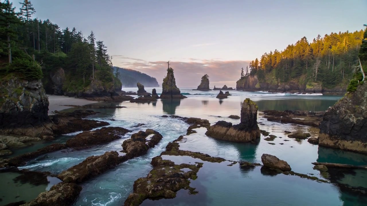 Descending camera revealing cove at low tide, exposing sea stacks and tidal channels for warm light