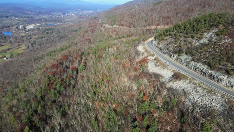 Drohnenaufnahmen-Einer-Malerischen-Bergautobahn-Mit-Wäldern-Und-Dem-Tal-Und-Ackerland-Darunter-Und-Bergen-Im-Hintergrund-Im-Herbst