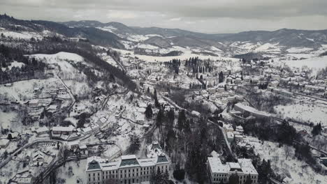 Amplia-Toma-Aérea-De-Una-Ciudad-Minera-Banska-Stiavnica-En-Invierno-Cubierta-De-Nieve,-Montañas-En-El-Fondo,-Nublado