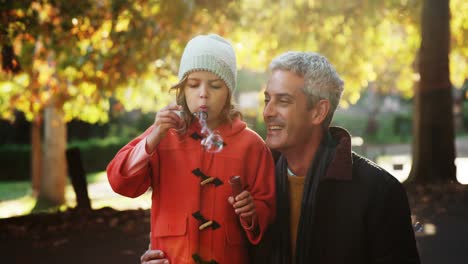 girl blowing bubbles held by dad outdoors