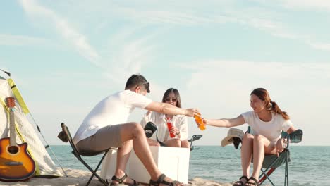 happy friends with drinks in camp and laughing together in holidays on sand beach near camping tent vacation time at sunset