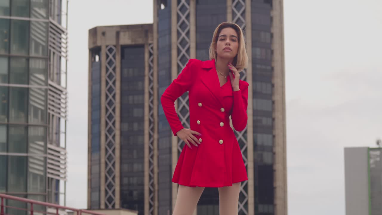 en el techo de un puerto de españa, una joven hispana en un vestido rojo contrasta contra el telón de fondo de los edificios altos