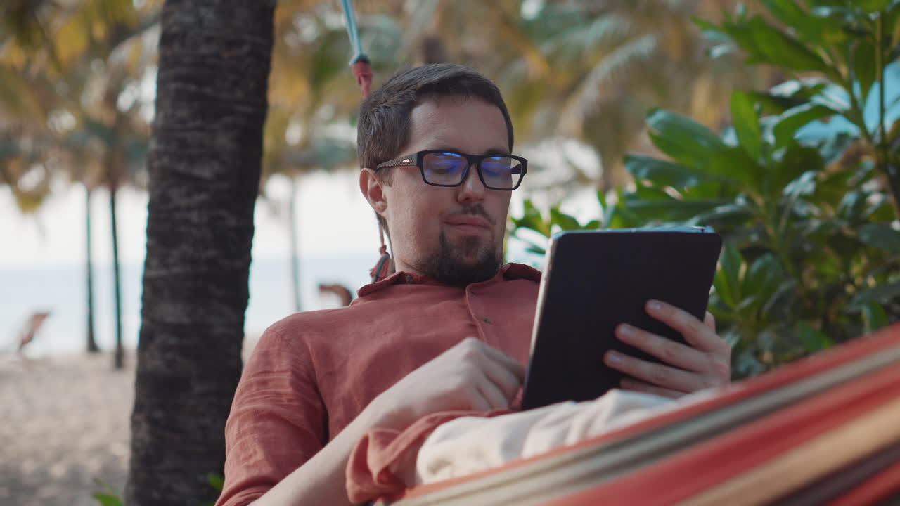 hombre relajándose en una hamaca en la playa con una tableta