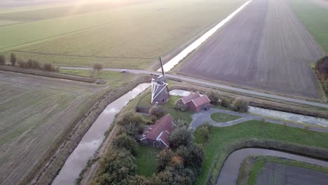 Observe-Cómo-El-Sol-Se-Esconde-Bajo-El-Horizonte,-Proyectando-Un-Cálido-Resplandor-Sobre-El-Pintoresco-Paisaje-Adornado-Con-Un-Molino-De-Viento-Tradicional.