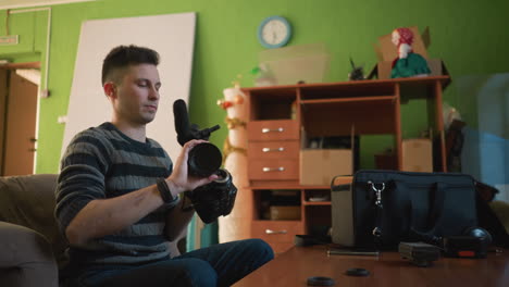 person adjusting camera setup in indoor workspace, preparing video equipment. microphone, camera, tripod, and gear placed on table. background includes green walls, office-like setting