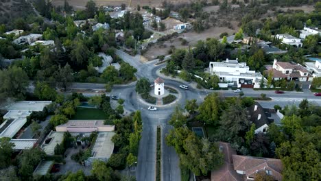 Aerial-Dolly-Beim-Absenken-Auf-Leonidas-Montes-Windmühle-Im-Kreisverkehr-Mit-Pendelnden-Fahrzeugen,-Umgeben-Von-Bäumen,-Lo-Barnechea,-Santiago,-Chile