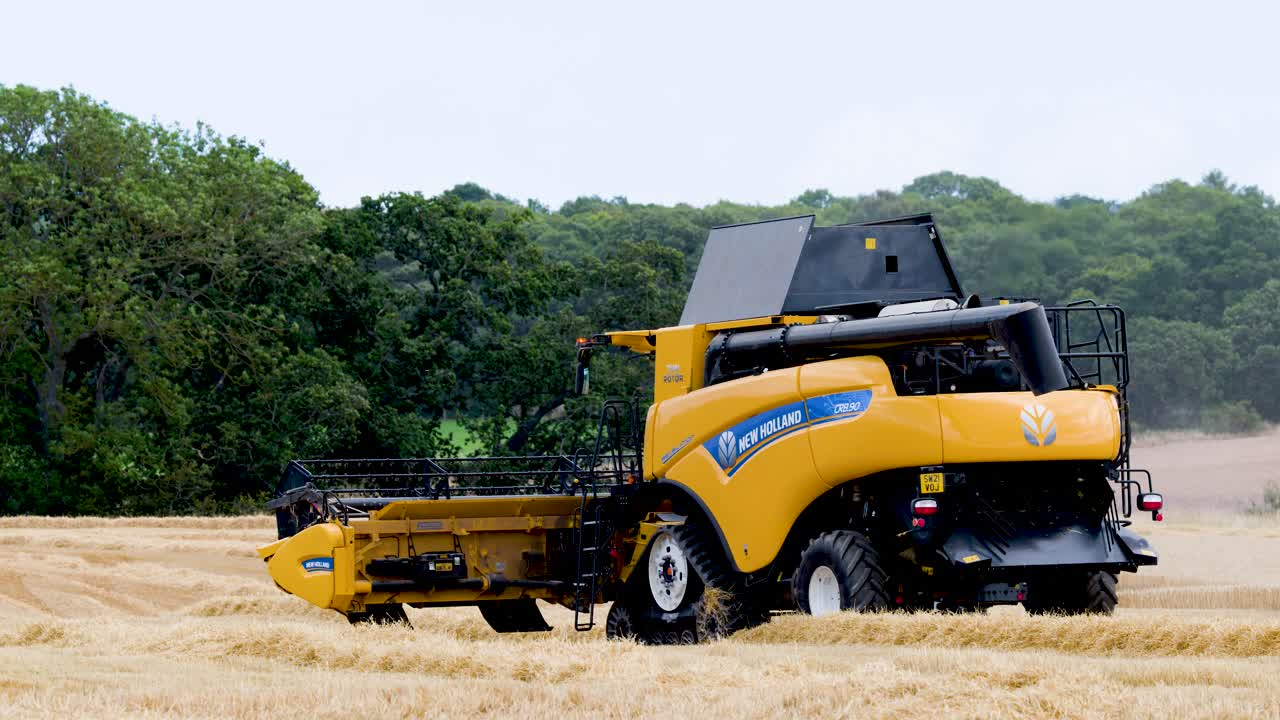 Yellow combine harvester harvesting crop in rural field, overcast daylight, static wide shot