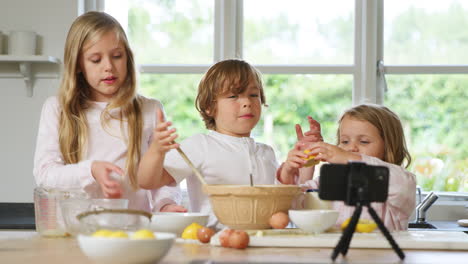 children in pyjamas baking in kitchen at home whilst vlogging on mobile phone