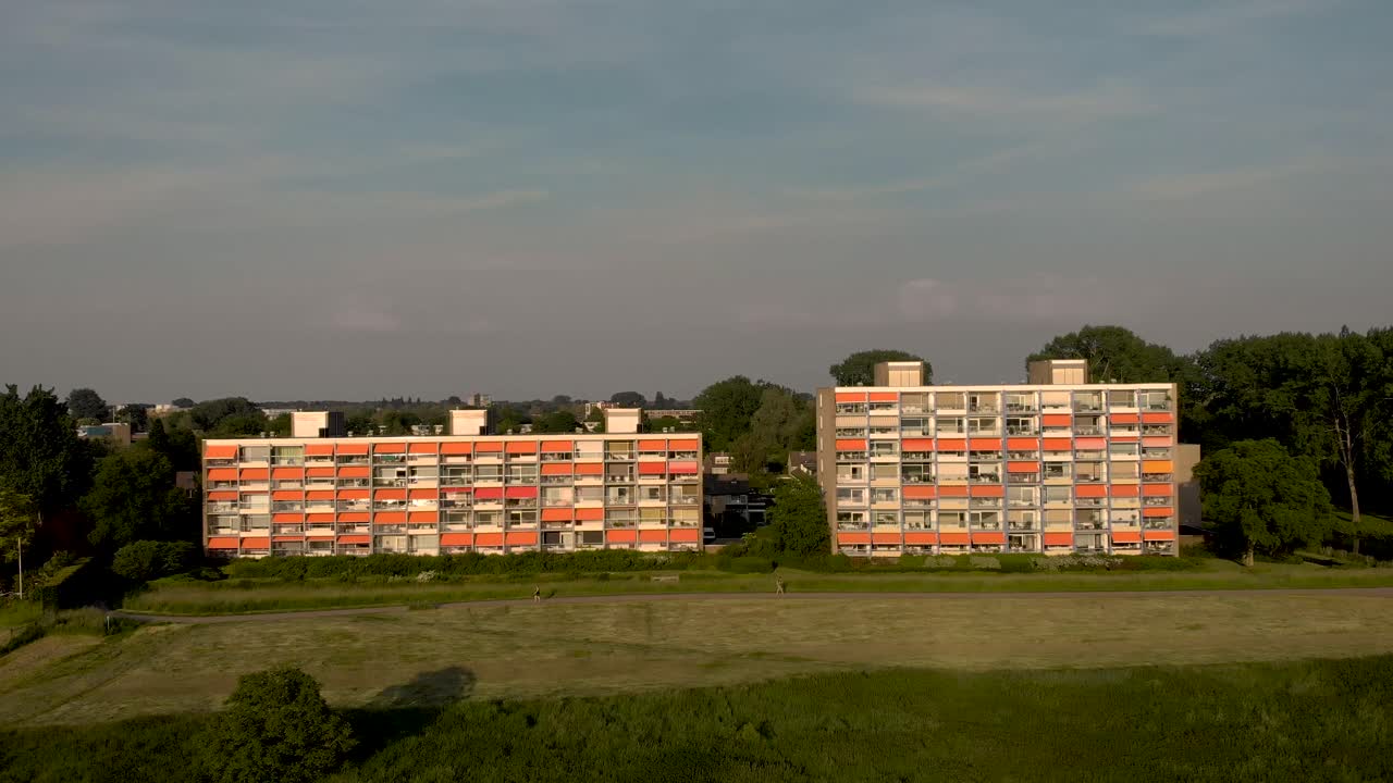 paisaje urbano aéreo al atardecer con edificios de apartamentos de gran altura con sombrilla naranja cerrada a lo largo del río ijssel en lento movimiento hacia atrás que revela el paisaje de las llanuras aluviales holandesas en zutphen, los países bajos