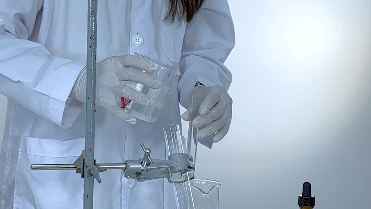 Uno scienziato versa attentamente un liquido in un contenitore di vetro utilizzando attrezzature da laboratorio.