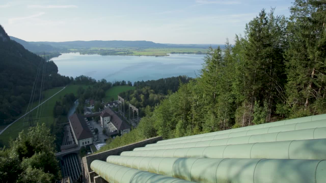vista elevada de grandes tuberías verdes con bosque y lago en el fondo, bajo un cielo despejado