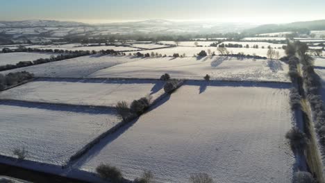 cold snowy winter british patchwork farmland countryside rural scene aerial at sunrise flyover slow