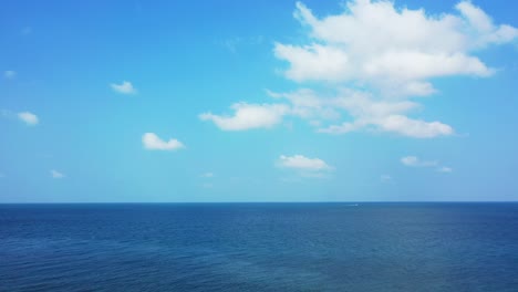 bright sky with white clouds over the deep blue ocean and one boat sailing on the horizon