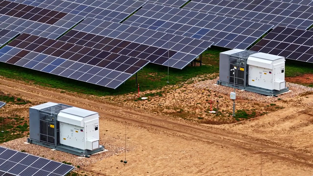 Due apparecchiature solari si trovano lungo un sentiero sterrato, circondate da un'ampia schiera di pannelli solari. La scena cattura l'infrastruttura dell'energia rinnovabile. Adatto per progetti ambientali ed energetici.
