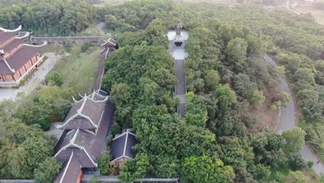 Drohnen-Luftaufnahme-In-Vietnam,-Die-Bei-Sonnenuntergang-über-Buddhistische-Tempelanlagen-Mit-Pagoden-Und-Mit-Grünen-Bäumen-Bedeckten-Straßen-In-Ninh-Binh-Fliegt