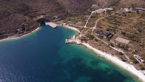 AERIAL-Fly-By-over-a-Turquoise-Beach-with-Abandoned-Communist-Structures-in-Albanian-Riviera