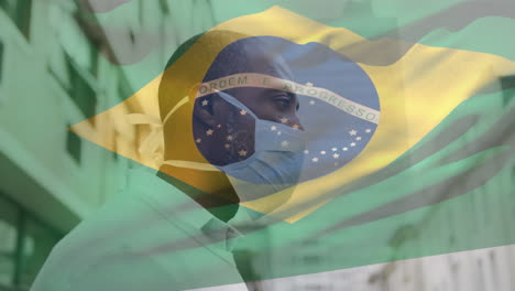 animation of flag of brazil waving over african american man wearing face mask in city street