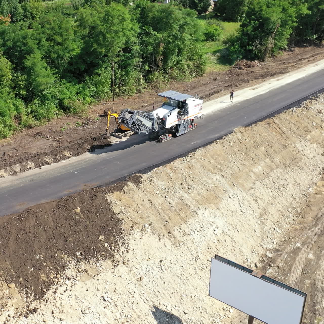 Roadworks of a new asphalt road. Modern machinery working on a road construction in summertime. Aerial view.