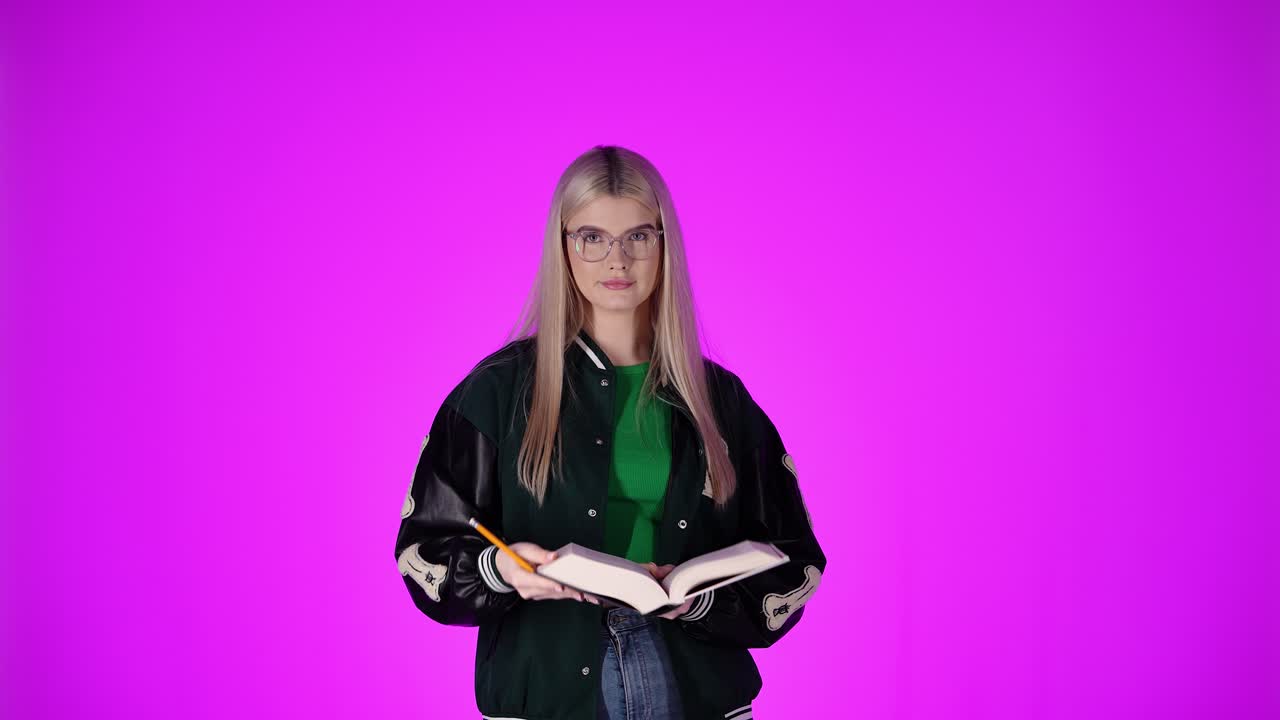 Donna bionda che prende appunti, chiude un libro e guarda la fotocamera, sfondo viola
