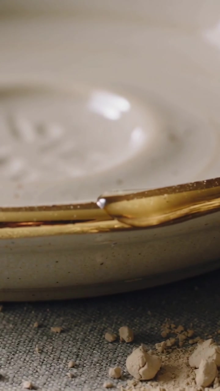 Video verticale: Goccia d'oro che scivola lungo il bordo di ceramica dorata per gravità su un panno con briciole