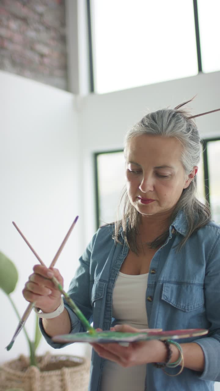 Video verticale: artista donna che guarda i pozzetti, mescolando la pittura verde sulla palette nel suo studio d'arte