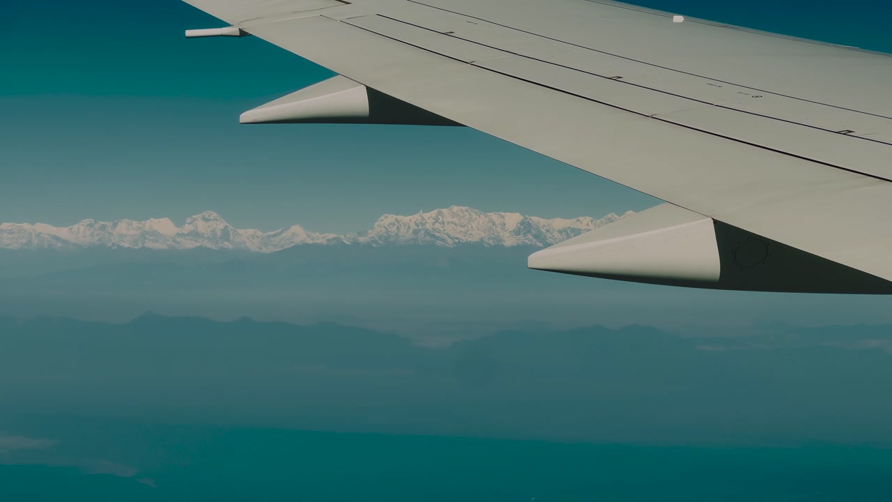 Airplane wing visible beside vast snow-covered Himalayan mountain range under clear blue sky, Nepal