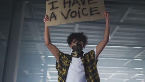 mixed race man wearing face mask holding protest placard in empty parking garage