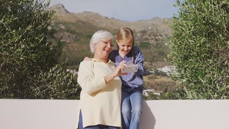 Grandmother-and-little-girl-happily-using-mobile-4K-4k