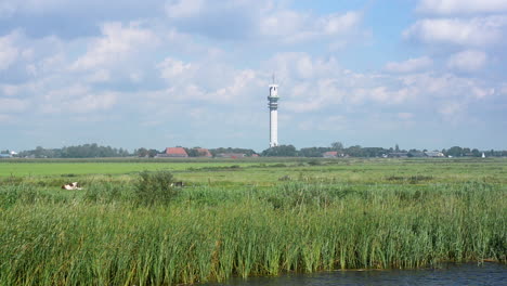 Flat-Dutch-landscape-with-tall-telecommunication-tower,-moving-shot-from-a-boat