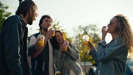 Young-people-in-trendy-clothes-stand-near-their-expensive-car-and-clink-glasses-with-yellow-cocktails.-Happy-life-in-the-urban