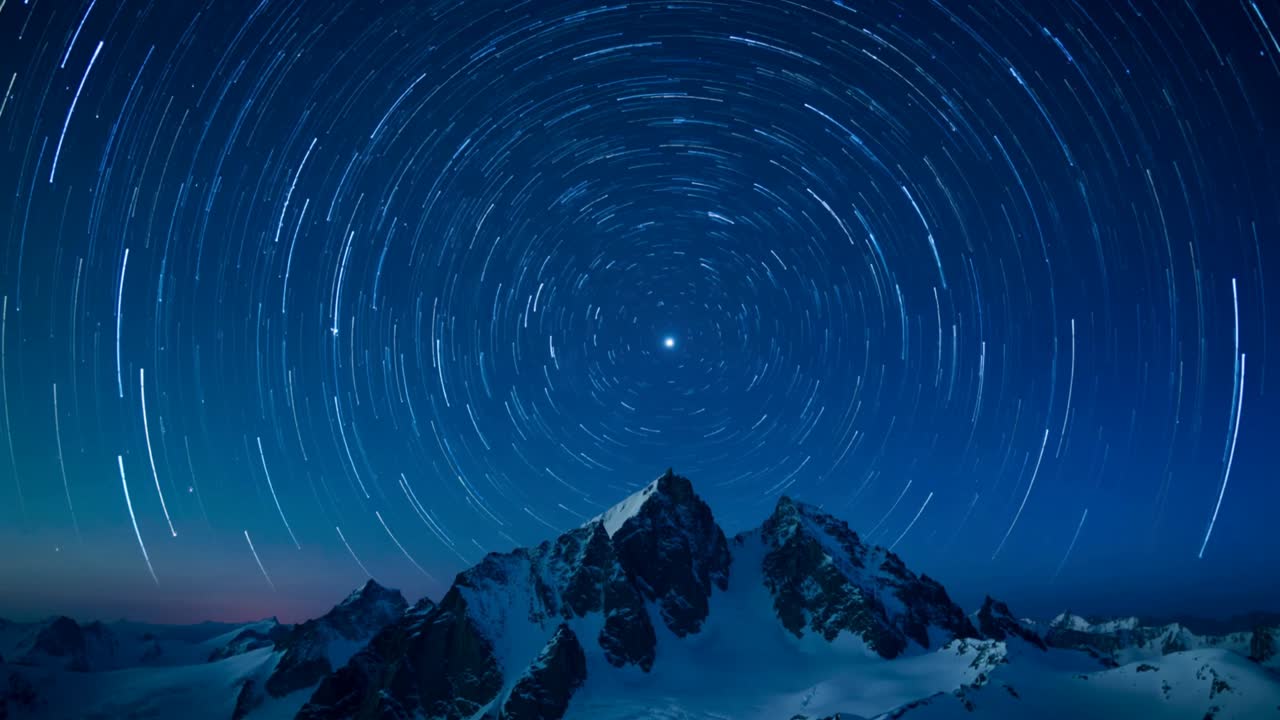 Die Kamera rahmt einen verschneiten Grat ein, während ein Zeitraffer Sternenringe festhält, die einen zentralen Stern umkreisen, begleitet von einem Polarlichtglühen.