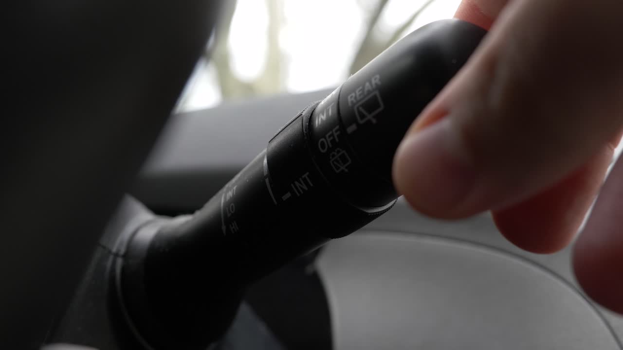 차 뒷면의 와이퍼 스위치를 휘두르는 하 백인 손의 극단적인 클로즈업