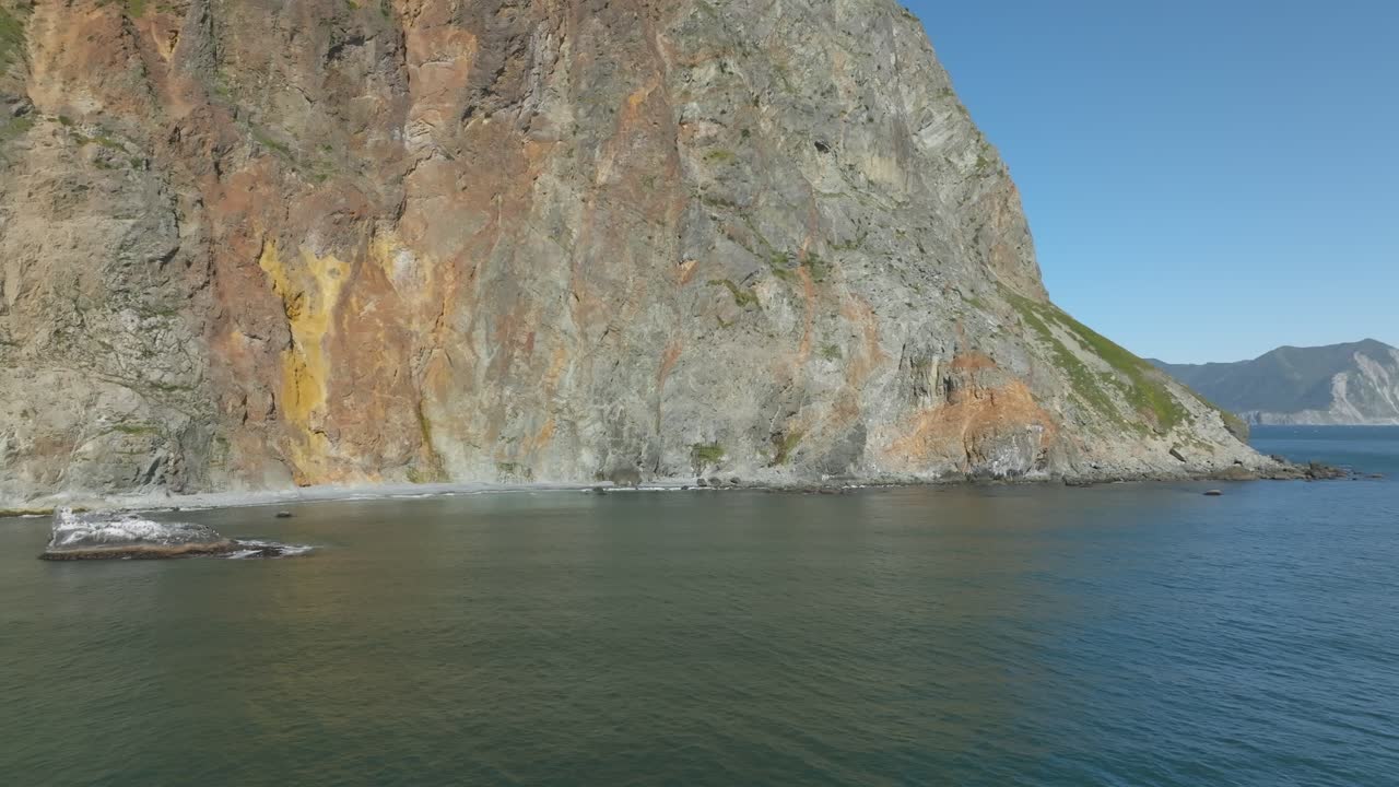 Aerial footage of steep volcanic sea cliffs and clear blue water along the remote coastline of Avacha Bay, Kamchatka Krai, Russia on a sunny summer day