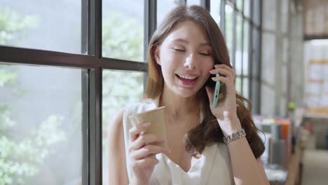 portrait of white caucasian female business woman using smartphone telecommunication in modern office,white caucasian standing hand hold coffee cup ahnd smartphone standing next to big window in offce