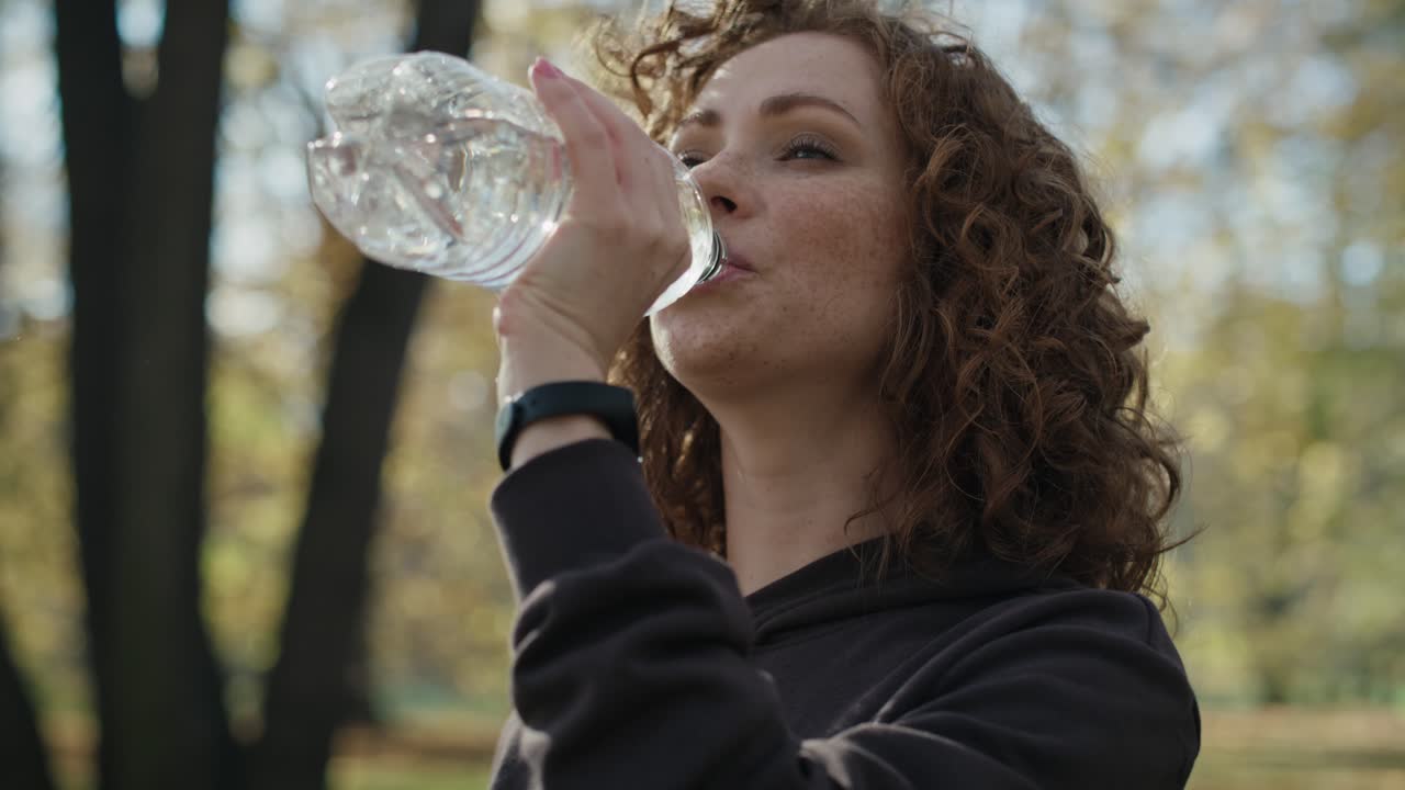 mujer de jengibre bebiendo agua durante el freno de trotar en el parque