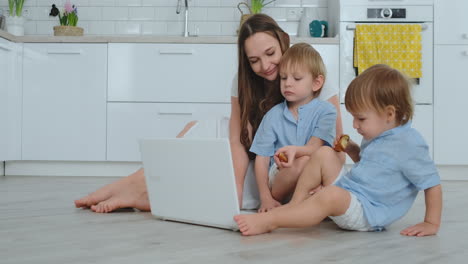 Moderne-Technologie.-Moderne-Wohnung-Liebende-Mutter-Und-Zwei-Kleine-Söhne-Sitzen-Auf-Dem-Boden-Im-Wohnzimmer-Und-Schauen-Auf-Den-Laptop-Bildschirm.-Kinder-Mit-Mama-Spielen-Auf-Einem-Laptop.