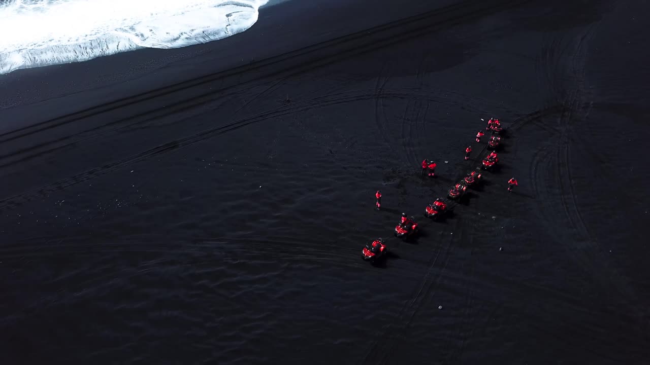 Aerial view of red quad bikes on Iceland black sand beach, next to the ocean