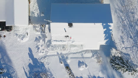 top down drone shot rising above a partly cleaned pv system on a snowy house roof