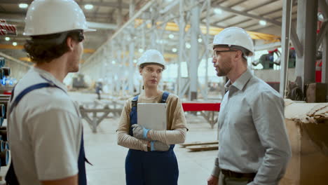 female factory worker talking with two male colleagues in industrial warehouse