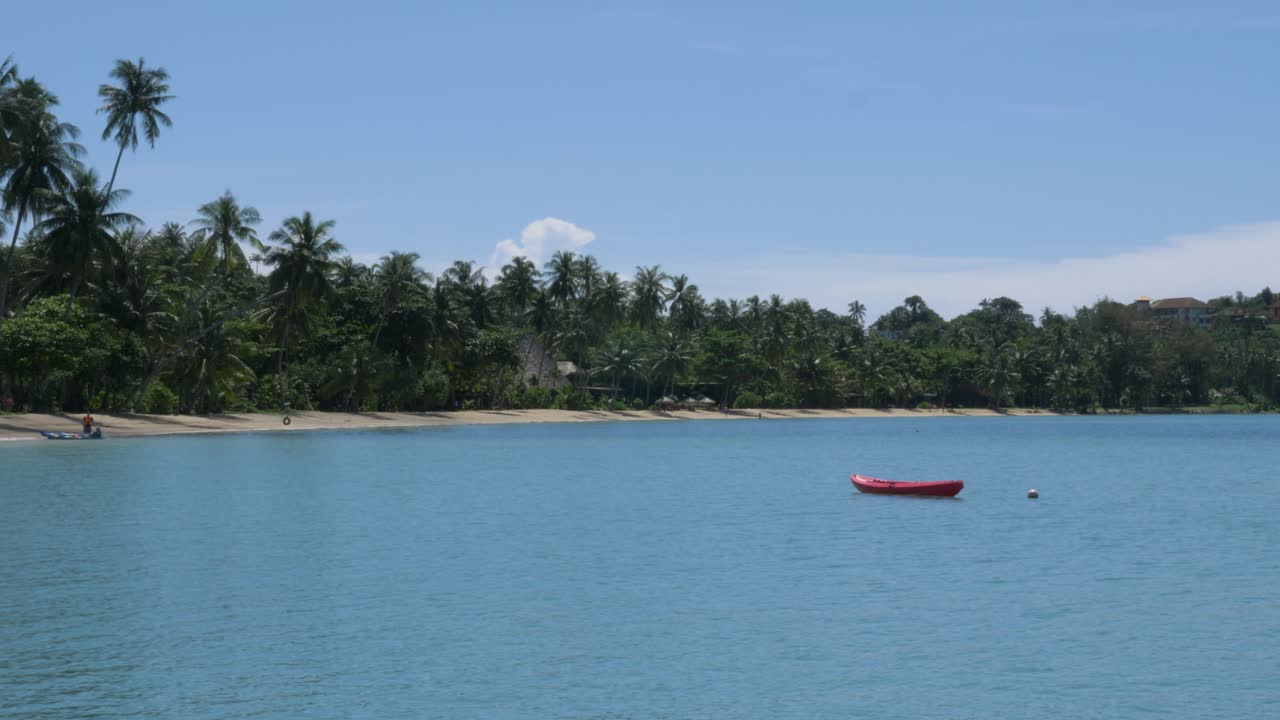 kayak rojo vacío balanceándose cerca de la orilla del océano de una playa remota en tailandia