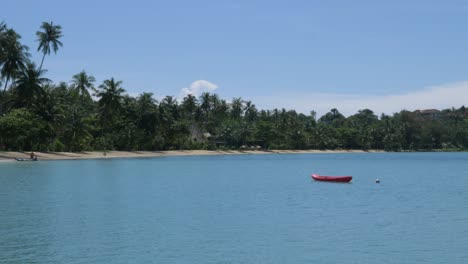 empty red kayak bobbing near the ocean shore of a remote beach in thailand