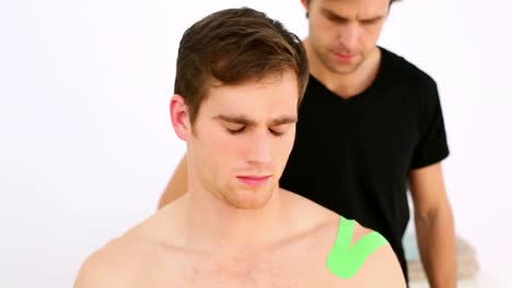 physiotherapist applying green kinesio tape to patients shoulder