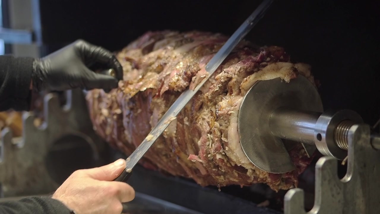 Chef che affetta carne appena arrostita da un girarrosto verticale