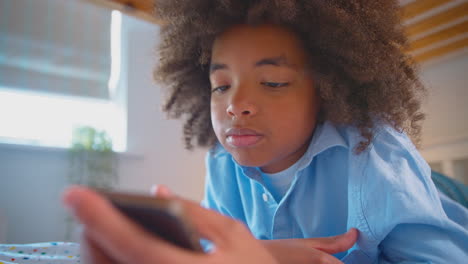 tired or worried boy in bedroom lying on bed holding mobile phone being bullied online