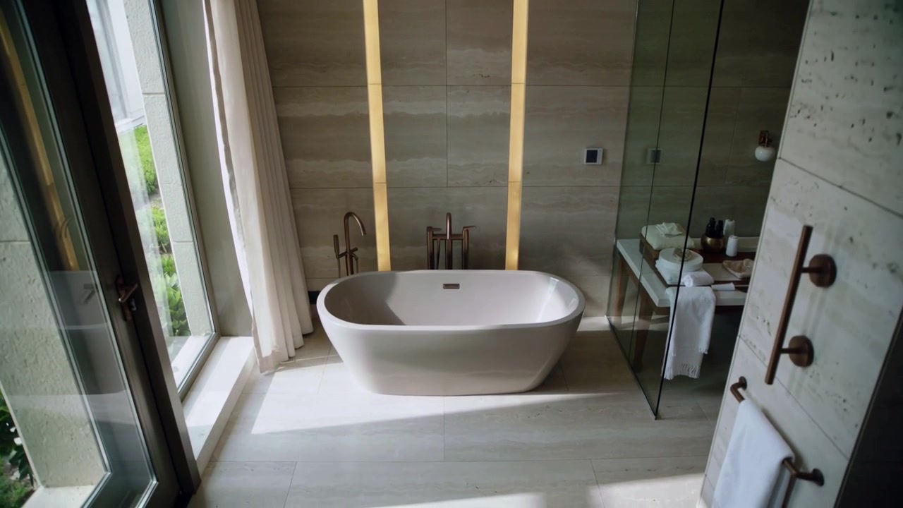 Telecamera che scende verso una vasca ovale autoportante nel bagno padronale, rivelando rubinetti e luce.