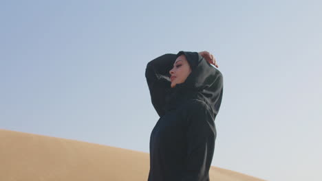 beautiful muslim woman wearing traditional black dress and hijab posing in a windy desert