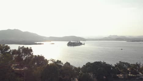 view-from-the-shore-of-Taj-Lake-Palace-in-Lake-Pichola-in-the-late-evening-mist,-in-Udaipur,-Rajasthan,-India---Aerial-slide-shot