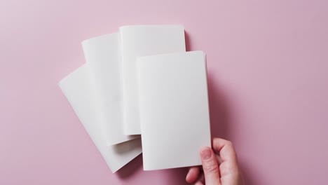 hand holding piece of paper over pieces of paper with copy space on pink background in slow motion